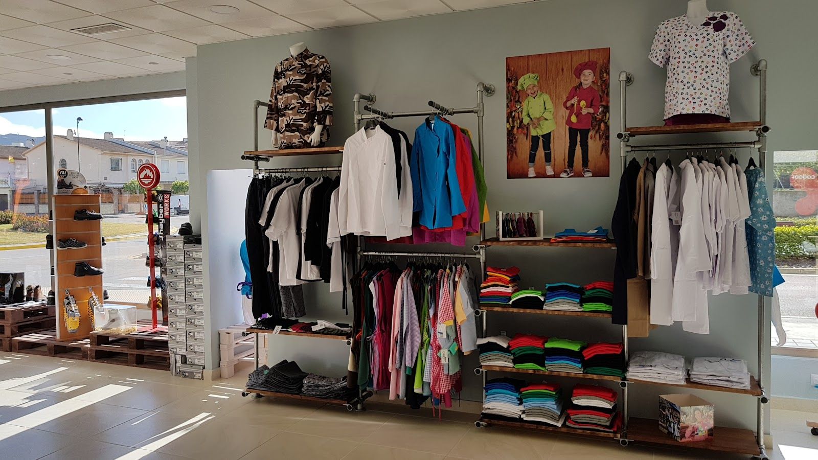 Interior de la tienda con percheros de uniformes sanitarios, batas blancas, chaquetillas de cocina y polos de trabajo