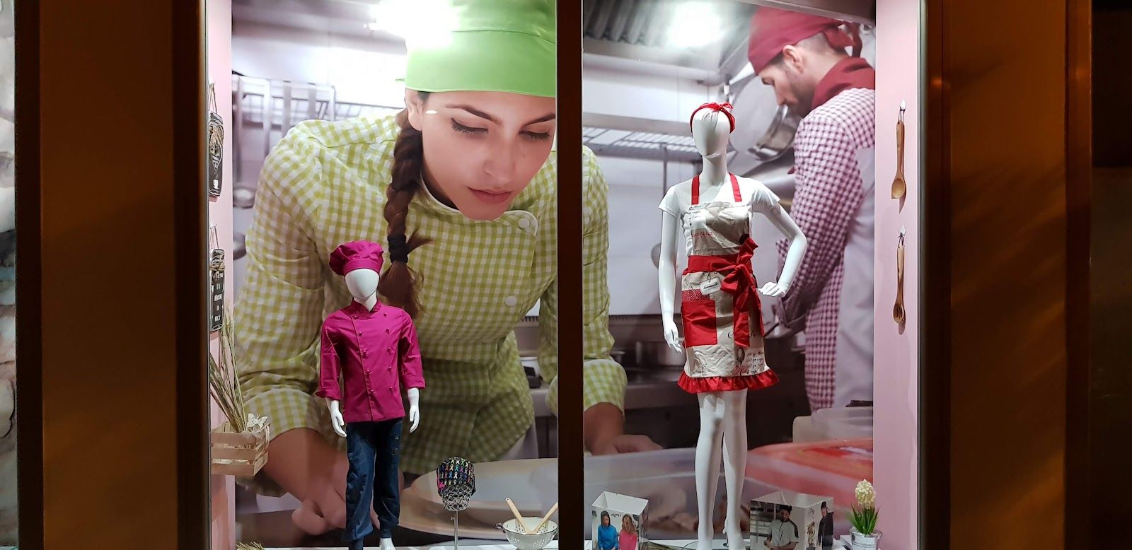 Escaparate temático de hostelería y cocina con chaquetillas de chef, delantales y mural de fondo culinario